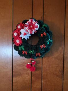 a green wreath with poinsettis and bells hanging on a wooden wall next to a door