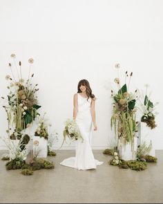 a woman standing in front of three tall vases filled with flowers and greenery