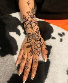 a woman's hand with black and white flowers tattooed on her left arm, sitting on a cow skin surface