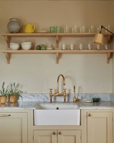 a kitchen with white cabinets and gold faucet, shelves above the sink are filled with dishes