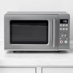 a silver microwave oven sitting on top of a white counter next to some cupboards