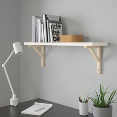 a desk with a lamp and some books on the shelf next to a potted plant