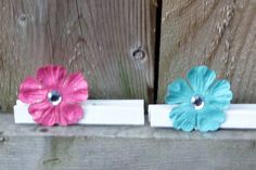 three flowers are placed on the side of a wooden fence, one pink and one blue