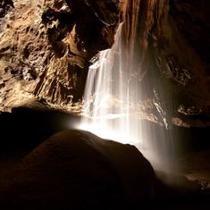 there is a waterfall in the middle of this cave with light coming from it's sides