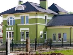 a large green house with black roof and white trim on the windows, fenced in area next to it