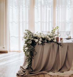 a table with flowers and candles on it in front of sheer drapes, next to a window