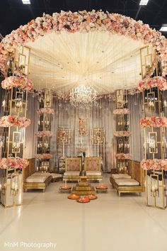 an elaborate wedding ceremony setup with flowers and chandelier in the middle, surrounded by gold chairs