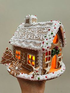 a gingerbread house decorated with icing and christmas decorations is being held by a hand