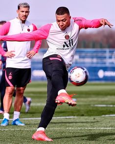 a man kicking a soccer ball on top of a grass covered field with other men in the background