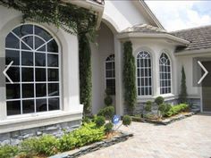 a large house with many windows and plants in front of the door, along with a brick driveway