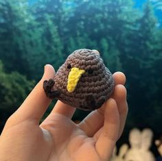 a hand holding a tiny crocheted bird in front of a green forest background