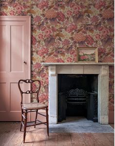 a chair sitting next to a fireplace in a room with floral wallpaper on the walls