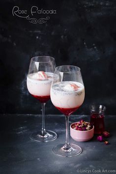 two wine glasses filled with ice cream and garnished with pink flowers on a dark surface