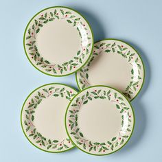 four green and white plates with holly designs on them, sitting next to each other