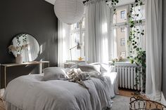 a white bed sitting in a bedroom next to a window filled with curtains and plants