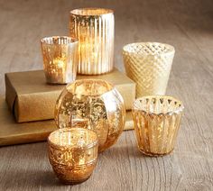 gold colored glass candlesticks and vases on a wooden table next to a book