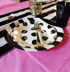 a black and white plate with gold polka dots on it sitting on a pink table cloth