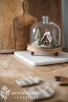 a miniature house under a glass clochet on top of a wooden table with other items