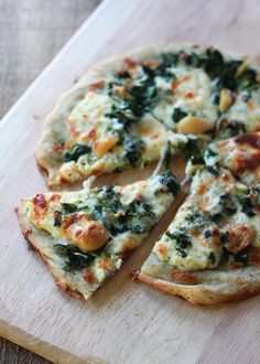 a pizza with cheese, spinach and other toppings on a wooden cutting board