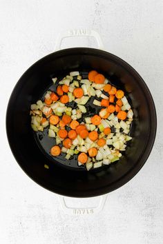 carrots, onions and celery cooking in a black skillet on a white surface