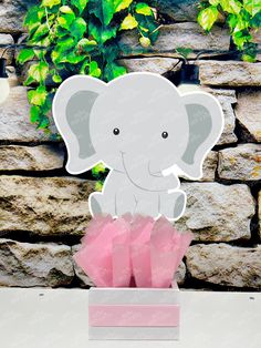 an elephant cutout sitting on top of a pink tissue paper box in front of a stone wall