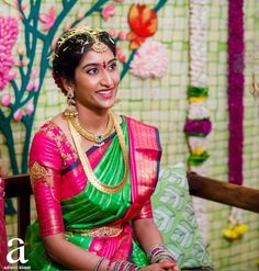 a woman in a green and pink sari sitting on a bench with flowers behind her