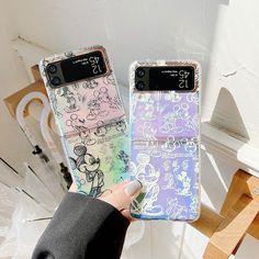 someone holding up two cell phones with mickey mouse designs on them, one is pink and the other is blue