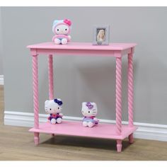 a pink table with two hello kitty stuffed animals on it's legs and a photo frame next to it