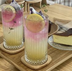 two glasses filled with different colored drinks sitting on top of a wooden tray next to each other