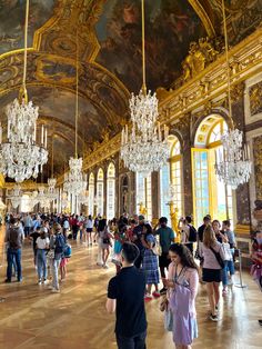 many people are walking around in a large room with chandeliers hanging from the ceiling