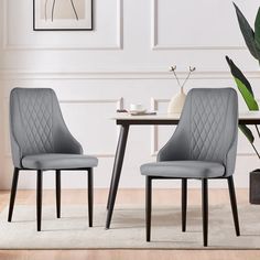 two gray chairs sitting next to each other on top of a rug in front of a table