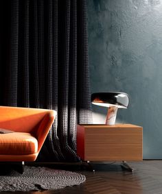 an orange couch sitting on top of a hard wood floor next to a black curtain