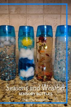 four different colored glass bottles sitting on top of a counter with snow and clouds in them