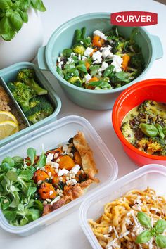 four plastic containers filled with food on top of a white table next to a potted plant