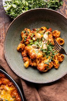 a plate of pasta with sauce and cheese on it next to a bowl of spinach