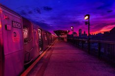 a train parked next to a street light at night with the sun setting in the background