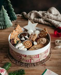 a christmas cookie tin with cookies and other treats in it on a wooden table next to decorations