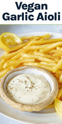 a white plate topped with french fries and a bowl of ranch dressing next to lemon wedges