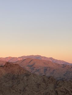 the mountains are covered in brown and pink hues as the sun sets over them