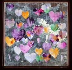 a window with hearts hanging from it's side and some flowers in the background