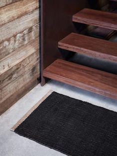 a black rug on the floor in front of a wooden wall with stairs leading up to it