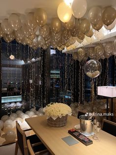 balloons are hanging from the ceiling above a dining room table with white flowers in a basket