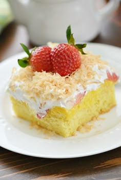 a piece of cake on a white plate with two strawberries on top and coconut flakes