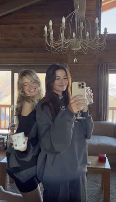 two women taking pictures with their cell phones in a living room, one holding a camera and the other looking at her phone