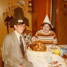 a man and woman sitting at a table with a turkey on it's head