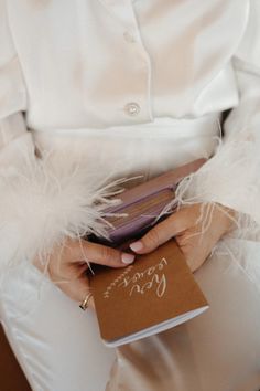 a woman in white holding a book with writing on it and feathers around her waist