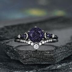 a purple diamond ring sitting on top of a black rock with white diamonds around it