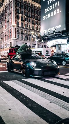 a black sports car driving down a street next to tall buildings in the city at night