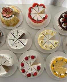 many different types of cakes on white plates with strawberries and cherries in the middle