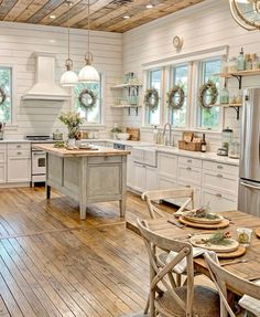 a kitchen with wooden floors and white cabinets, an island table surrounded by wreaths